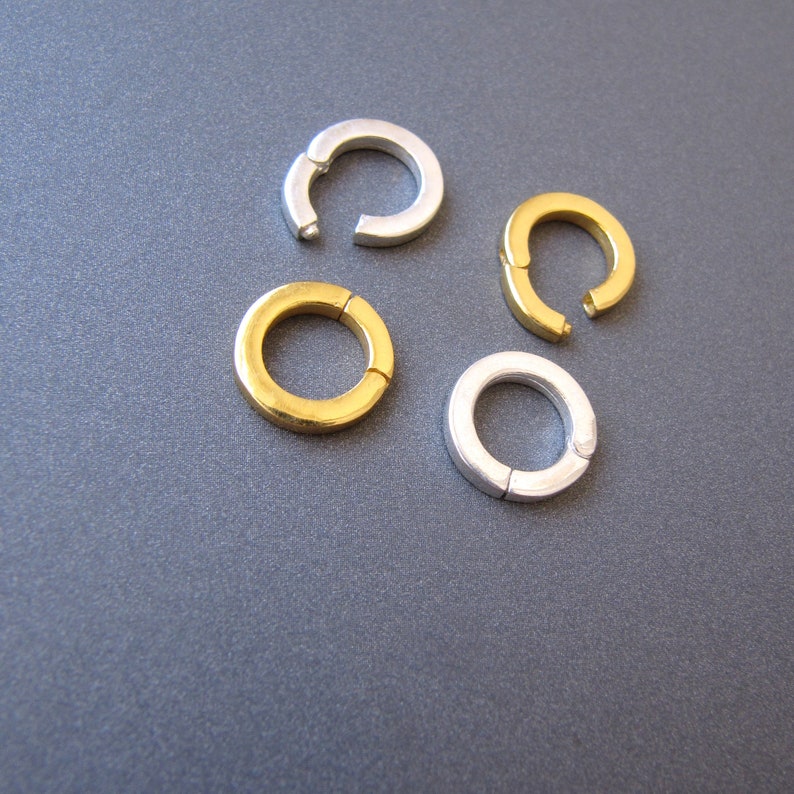 May include: Four jump rings, two silver and two gold, are arranged on a gray surface. The rings are open and ready to be used for jewelry making.