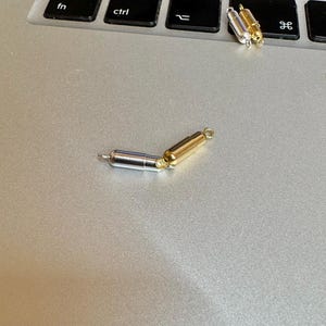 May include: A silver and gold magnetic clasp for a necklace or bracelet. The clasp is made of two pieces that connect together with magnets.