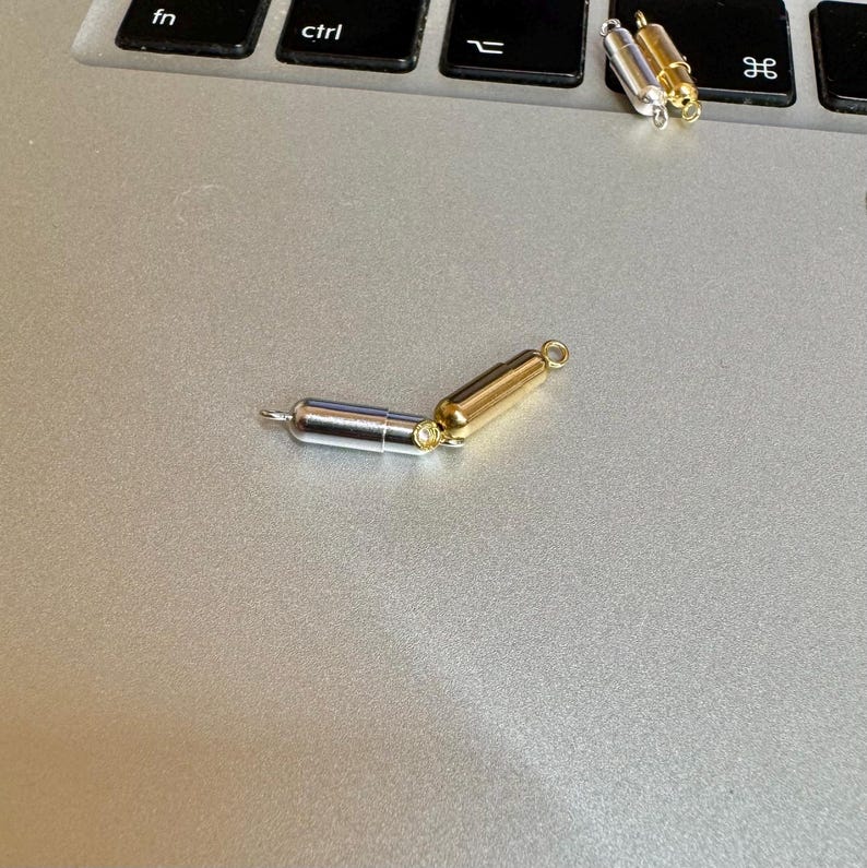 May include: A silver and gold magnetic clasp for a necklace or bracelet. The clasp is made of two pieces that connect together with magnets.