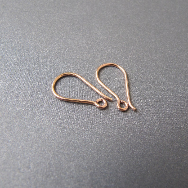 May include: Two rose gold earring hooks. The hooks are made of metal and have a teardrop shape.