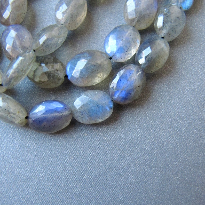 May include: A strand of oval-shaped labradorite beads with a blue iridescent sheen. The beads are strung on a black cord.