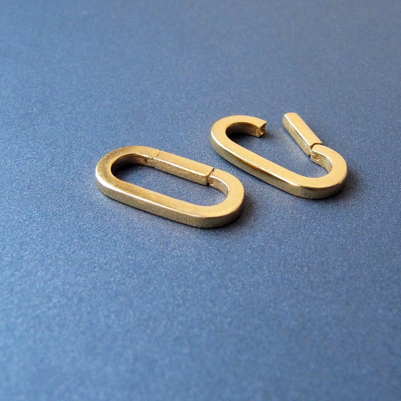 May include: Two gold-toned metal oval-shaped clasps. The clasps are open and ready to be attached to a chain or other jewelry.