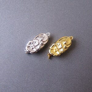 May include: Two metal flower-shaped clasps, one silver and one gold, for necklaces or bracelets.