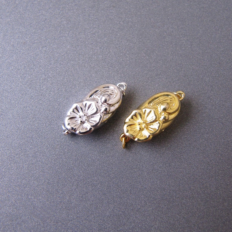 May include: Two metal flower-shaped clasps, one silver and one gold, for necklaces or bracelets.
