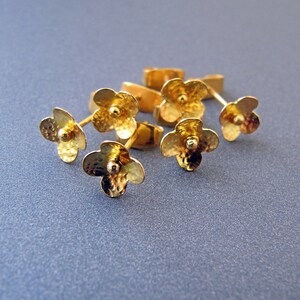 K&ouml;nnte beinhalten: F&uuml;nf goldene Ohrringe in Bl&uuml;tenform mit strukturierter Oberfl&auml;che. Die Ohrringe sind mit einer kleinen runden Perle in der Mitte jeder Bl&uuml;te verziert.