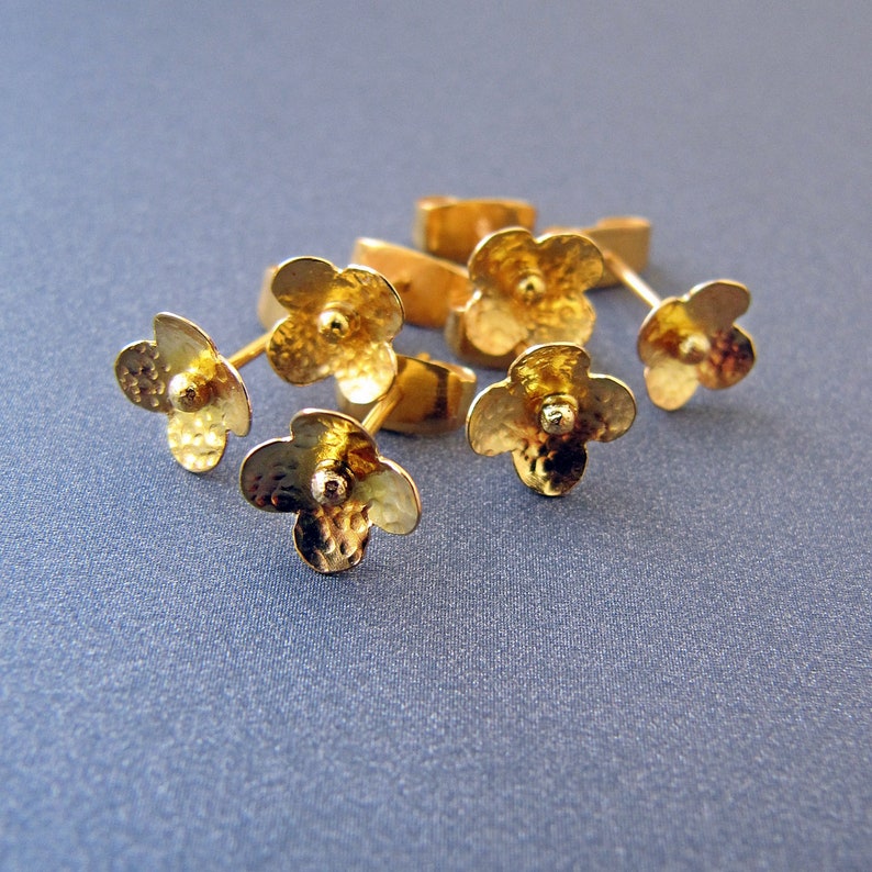 K&ouml;nnte beinhalten: F&uuml;nf goldene Ohrringe in Bl&uuml;tenform mit strukturierter Oberfl&auml;che. Die Ohrringe sind mit einer kleinen runden Perle in der Mitte jeder Bl&uuml;te verziert.