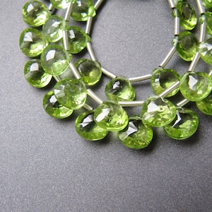 May include: A strand of green peridot gemstone beads strung on silver wire. The beads are faceted and have a teardrop shape.
