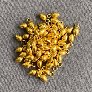 May include: A pile of gold-coloured metal teardrop-shaped charms with a loop at the top. The charms are approximately 2.5 cm long and are ideal for jewellery making.