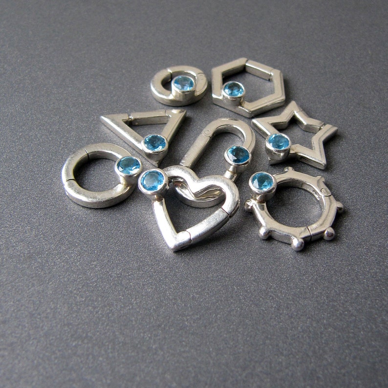 May include: A set of silver charm pendants with blue gemstones in various geometric shapes, including a heart, a circle, a star, a triangle, and a hexagon.