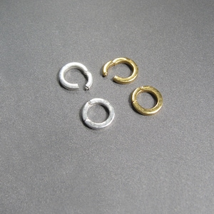 May include: Four jump rings, two silver and two gold, on a gray background.