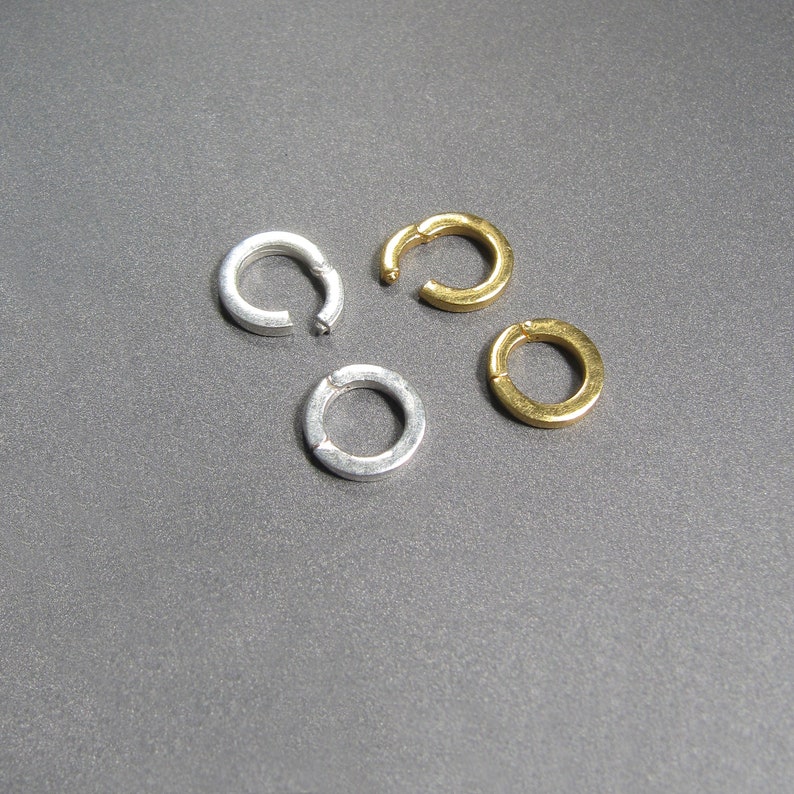 May include: Four jump rings, two silver and two gold, on a gray background.