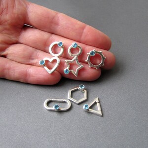 May include: A set of six silver charms with blue gemstones. Each charm is a different geometric shape: a circle, a heart, a star, a hexagon, a rectangle, and a triangle.