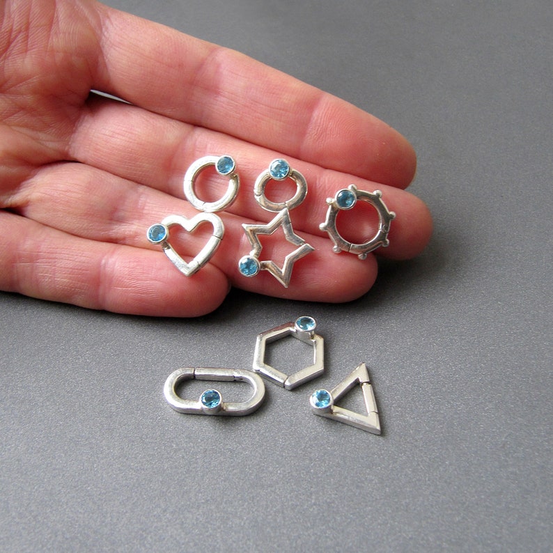 May include: A set of six silver charms with blue gemstones. Each charm is a different geometric shape: a circle, a heart, a star, a hexagon, a rectangle, and a triangle.
