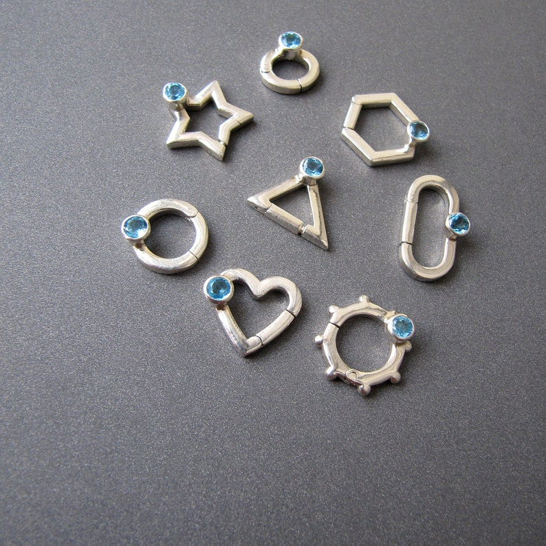 May include: Ten silver charms with blue gemstones, each charm is a different geometric shape: circle, star, heart, hexagon, triangle, and oval.