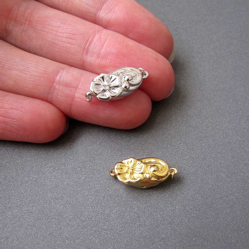May include: Two flower-shaped clasps for jewelry making. One is silver and the other is gold.