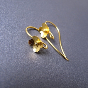 May include: A pair of gold-colored flower earrings. Each earring features a small, three-dimensional flower with delicate petals. The earrings have a curved hook design for pierced ears, and are displayed against a dark gray background.