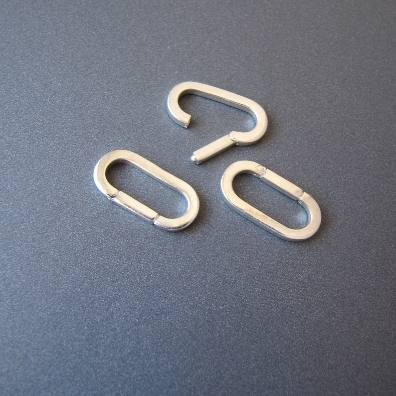 May include: Three silver metal oval-shaped jump rings. The rings are open and have a smooth finish.