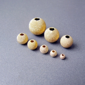 May include: A set of eight gold-coloured beads with a textured surface. The beads are arranged in a pyramid shape, with the largest bead at the top and the smallest bead at the bottom.