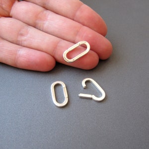 May include: Three silver jump rings, two are oval shaped and one is a hook shape.
