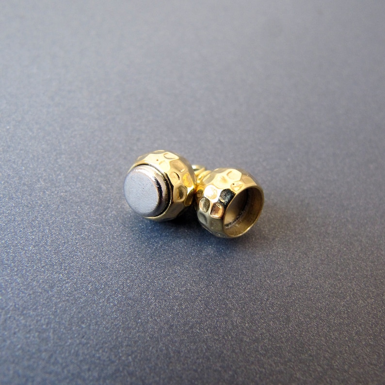 Op de afbeelding: Twee goudkleurige metalen kralen met een gehamerde textuur. E&eacute;n kraal heeft een zilverkleurige kern.
