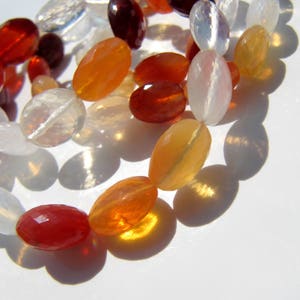 May include: A strand of oval-shaped gemstone beads in various colors, including white, orange, red, and yellow. The beads are strung on a clear cord and are arranged in a loose, flowing pattern.