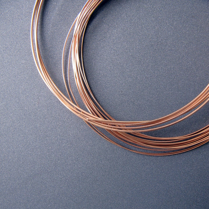 May include: A close-up of a bundle of copper wire, coiled in a circular shape, against a gray background.