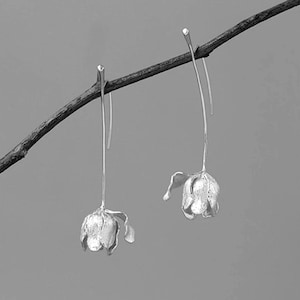 May include: A pair of silver dangle earrings with a flower design. The earrings are hanging from a branch.