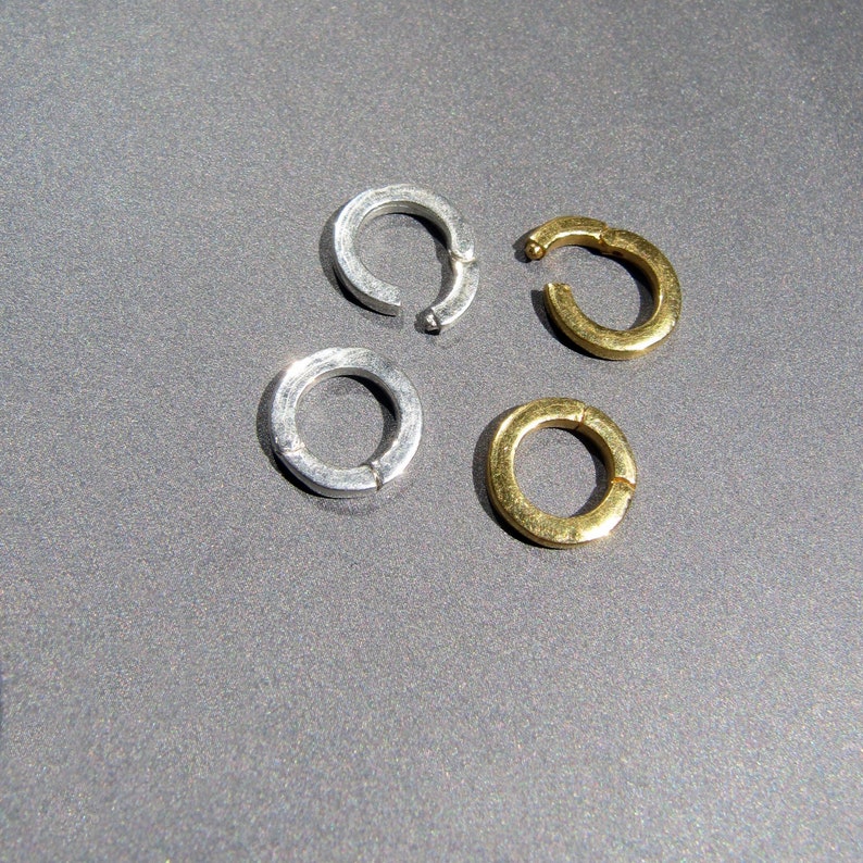 May include: Four metal rings, two silver and two gold, are arranged on a gray surface. The rings are all open and have a circular shape.