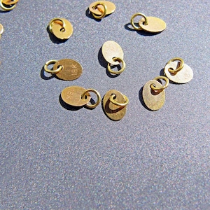 Etiqueta de oro de 18k • Disco plano ovalado de 3,6x5 mm • Anillo abierto de 3 mm con orificio de 2 mm • Dije pequeño • Oro macizo de 18 quilates • Sello estampado