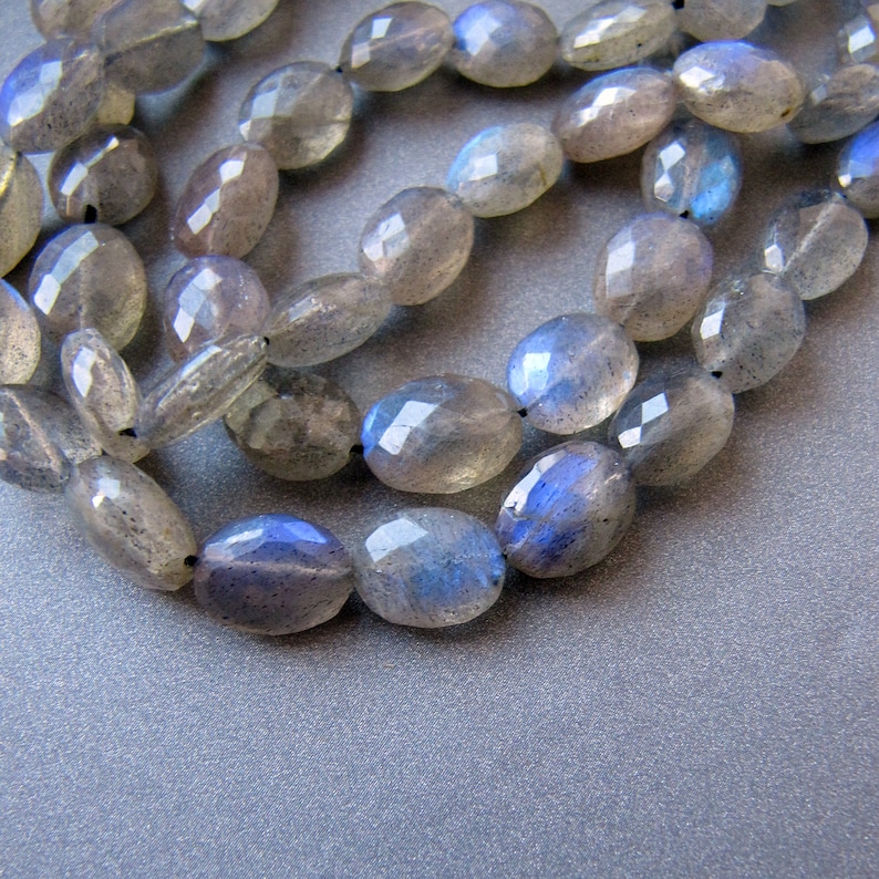 May include: A strand of oval-shaped, faceted labradorite beads with a blue iridescent sheen. The beads are strung on a clear thread and are arranged in a loose, overlapping pattern.