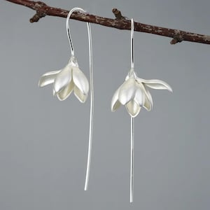 Könnte beinhalten: Ein Paar silberne Ohrringe mit filigranen Blumenanhängern. Die Ohrringe sind lang und schmal, mit einem schlichten Design.