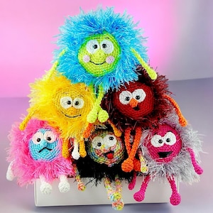 May include: A group of six colorful crocheted plush toys with different facial expressions. The toys are arranged in a pyramid shape and have long, thin arms and legs.