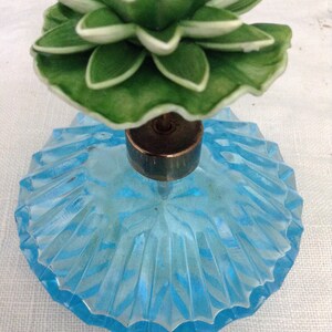 K&ouml;nnte beinhalten: Eine vintage Parf&uuml;mflasche aus blauem Glas mit einem gr&uuml;nen und wei&szlig;en Blumenverschluss.
