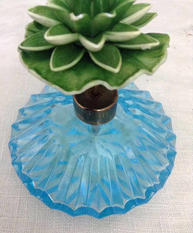 K&ouml;nnte beinhalten: Eine vintage Parf&uuml;mflasche aus blauem Glas mit einem gr&uuml;nen und wei&szlig;en Blumenverschluss.