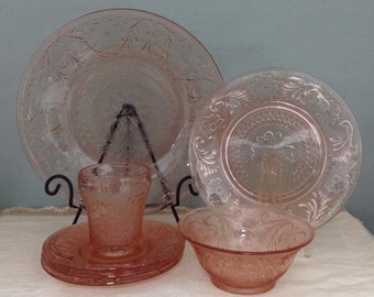 Könnte beinhalten: Set aus rosa Depression Glass Geschirr, bestehend aus einem großen Teller, einem kleineren Teller, einer Schüssel und einem Glas. Das Geschirr hat ein zartes Blumenmuster.