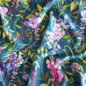 May include: Teal blue fabric with a floral pattern of pink, purple, and white wisteria flowers. The fabric has a silky sheen and is perfect for crafting projects.