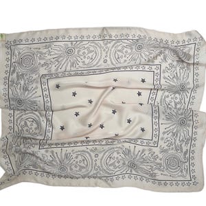 May include: Off-white square scarf with a celestial design. The scarf features a border of stars and suns, with additional stars scattered across the center. The design is in black ink on the off-white fabric.