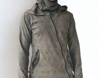 May include: An olive green long-sleeve hooded jacket featuring a dark geometric pattern, an asymmetrical front zip, a high neck collar, and thumbhole cuffs, paired with dark grey athletic shorts and black leggings.