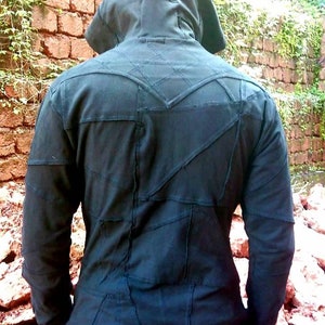 May include: A black hooded jacket with a patchwork design. The jacket is made of multiple pieces of fabric sewn together, creating a unique and textured look.