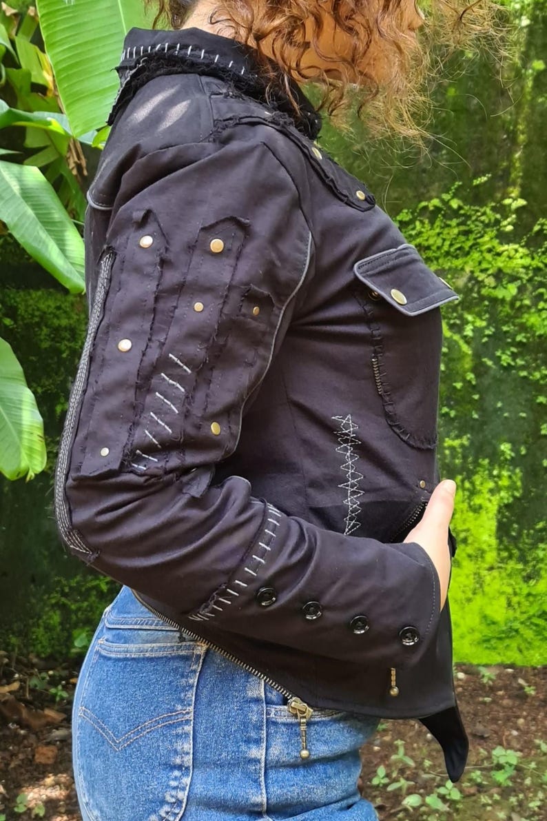 Puede incluir: Una chaqueta negra con cuello alto y costuras blancas en contraste, tachuelas met&aacute;licas doradas en las mangas, un bolsillo en el pecho con solapa y botones negros en los pu&ntilde;os. La chaqueta incluye costuras decorativas en zigzag de color blanco.