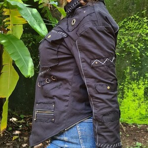 Puede incluir: Una chaqueta negra con dobladillo asim&eacute;trico, m&uacute;ltiples bolsillos con cremalleras y solapas, ojales met&aacute;licos y costuras decorativas blancas a lo largo de las costuras. La chaqueta incluye detalles de tela desgastada y una cremallera frontal.