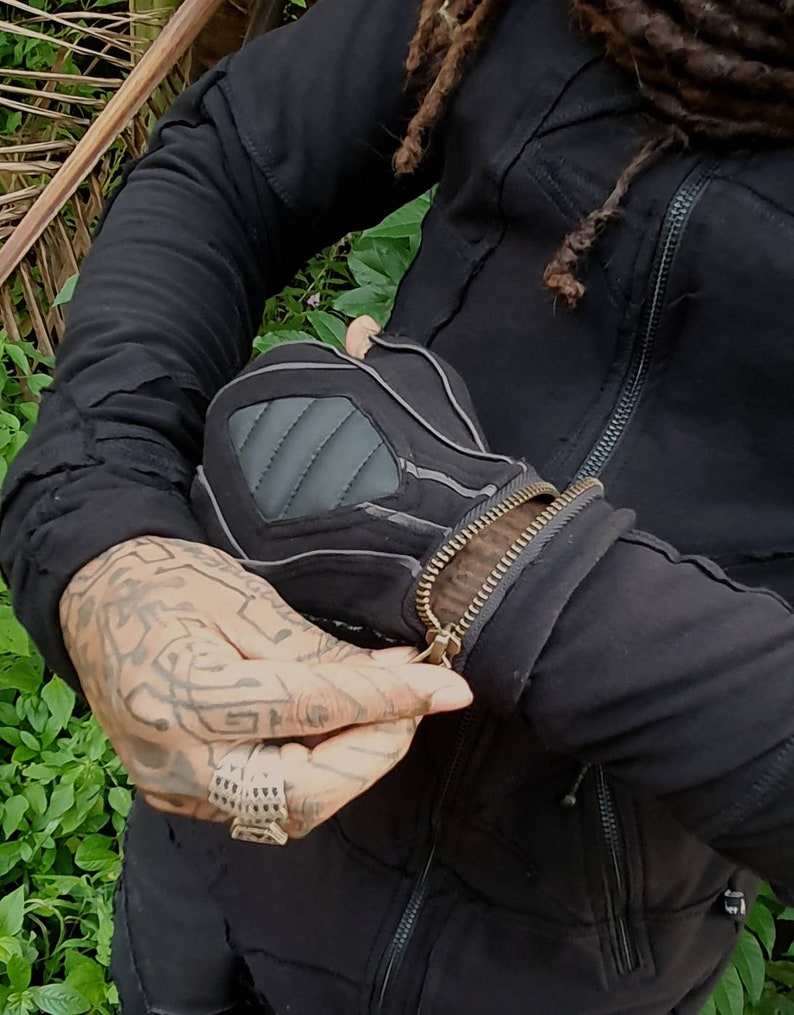 May include: A black jacket with a zip closure and multiple pockets. The jacket has a distressed look with visible stitching and seams. The zip is partially open, revealing a black and grey inner lining.