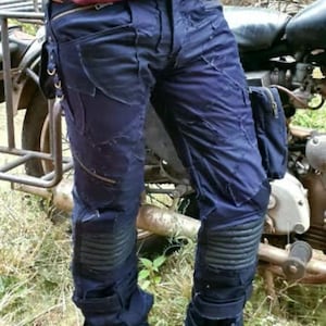 Może przedstawiać: Ciemnoniebieskie dżinsowe spodnie z wieloma kieszeniami i paskami. Spodnie mają ochraniacze na kolana i są noszone z czarnymi butami.