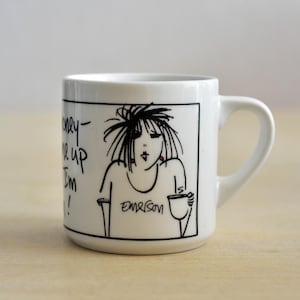 K&ouml;nnte beinhalten: Wei&szlig;e Keramiktasse mit einer schwarz-wei&szlig;en Cartoon-Illustration einer Frau, die eine Tasse h&auml;lt. Die Tasse hat einen gebogenen Henkel und der Text "Honey, wake up I'm in!" ist auf der Seite geschrieben.