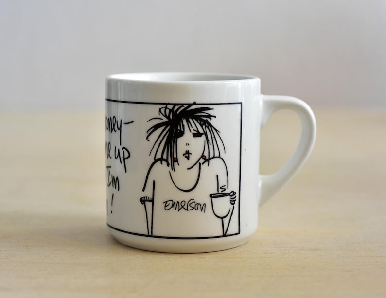 K&ouml;nnte beinhalten: Wei&szlig;e Keramiktasse mit einer schwarz-wei&szlig;en Cartoon-Illustration einer Frau, die eine Tasse h&auml;lt. Die Tasse hat einen gebogenen Henkel und der Text "Honey, wake up I'm in!" ist auf der Seite geschrieben.
