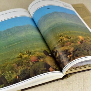 May include: An open book with a photograph of soldiers in a military setting. The book's title is "Tactics".