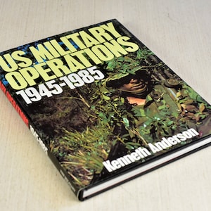 Pode incluir: Um livro intitulado "US Military Operations 1945-1985" de Kenneth Anderson. A capa apresenta uma foto de um soldado em camuflagem, segurando um rifle, em um cen&aacute;rio de selva.