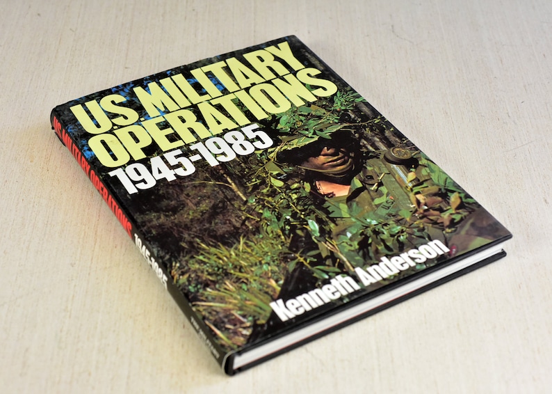 Pode incluir: Um livro intitulado "US Military Operations 1945-1985" de Kenneth Anderson. A capa apresenta uma foto de um soldado em camuflagem, segurando um rifle, em um cen&aacute;rio de selva.