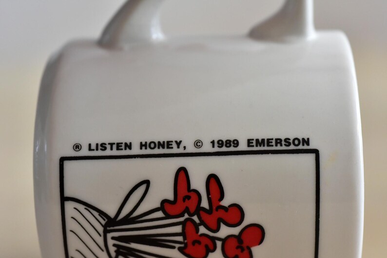 K&ouml;nnte beinhalten: Wei&szlig;er Keramikbecher mit Henkel, mit dem Text "LISTEN HONEY, &copy; 1989 EMERSON". Der Becher hat einen schwarzen Rand um eine Grafik roter Blumen. Ein Vintage-Sammlerst&uuml;ck.