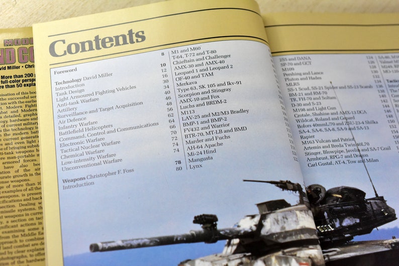 May include: A close-up of a book titled "Modern Fighting Vehicles" with a table of contents listing various military vehicles, including tanks, armored fighting vehicles, helicopters, and aircraft. The book is open to a page with a picture of a tank.
